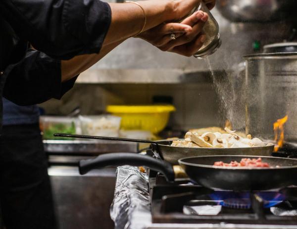 Glockna chef seasoning mushrooms in a pan on gas stove in professional kitchen