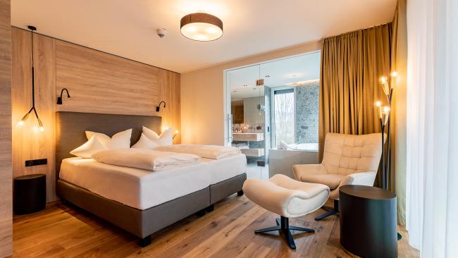 Modernes Schlafzimmer im Pfalzblick Wald Spa Resort mit Holzfußboden und gemütlichem Sessel