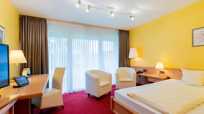 Gemütliches Hotelzimmer im Pfalzblick Wald Spa Resort mit gelben Wänden und rotem Teppich