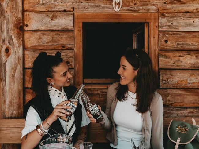 Two women toast in a rustic wooden cabin; Hotel Jagdhof Pfurtscheller