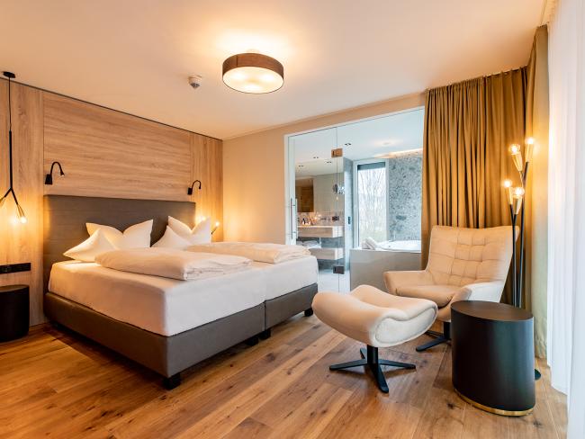Modernes Schlafzimmer im Pfalzblick Wald Spa Resort mit Holzfußboden und gemütlichem Sessel