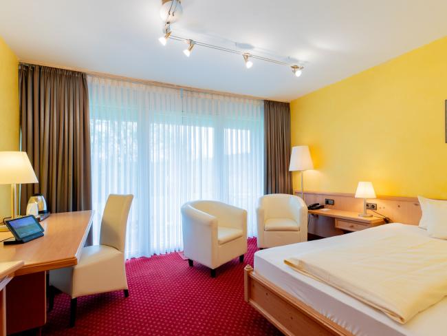 Gemütliches Hotelzimmer im Pfalzblick Wald Spa Resort mit gelben Wänden und rotem Teppich