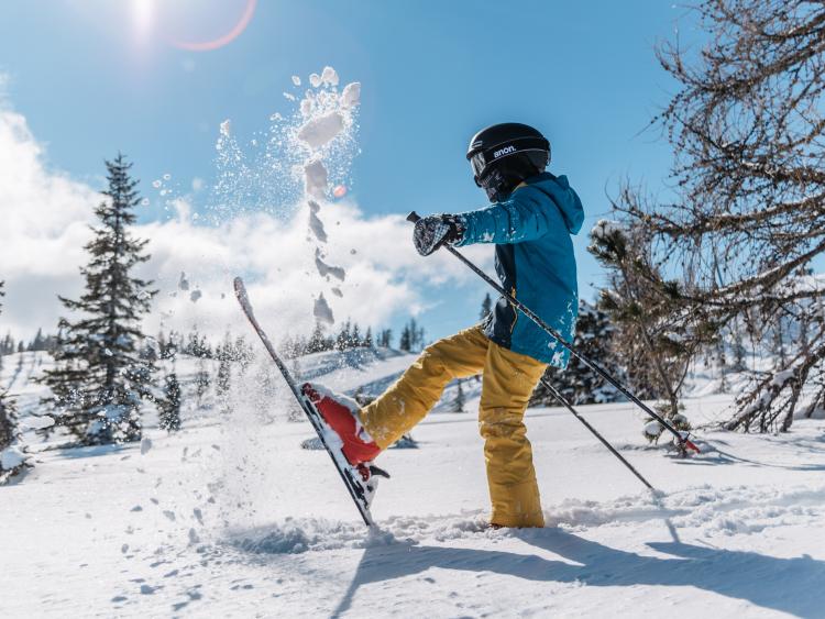 Skifahrer wirbelt Schnee auf einer sonnigen Piste beim Hotel Forstauerwirt auf