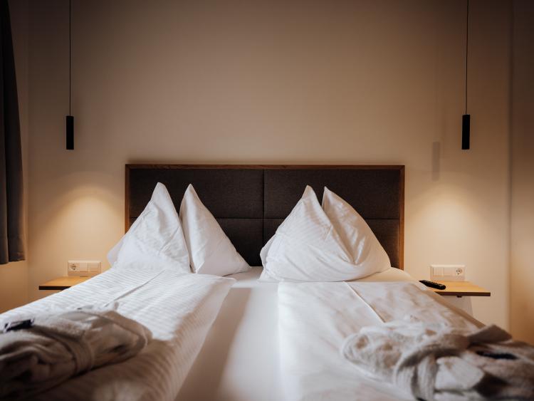 Gepflegtes Doppelbett im Hotel Forstauerwirt mit weißen Kissen und gefalteten Bademänteln