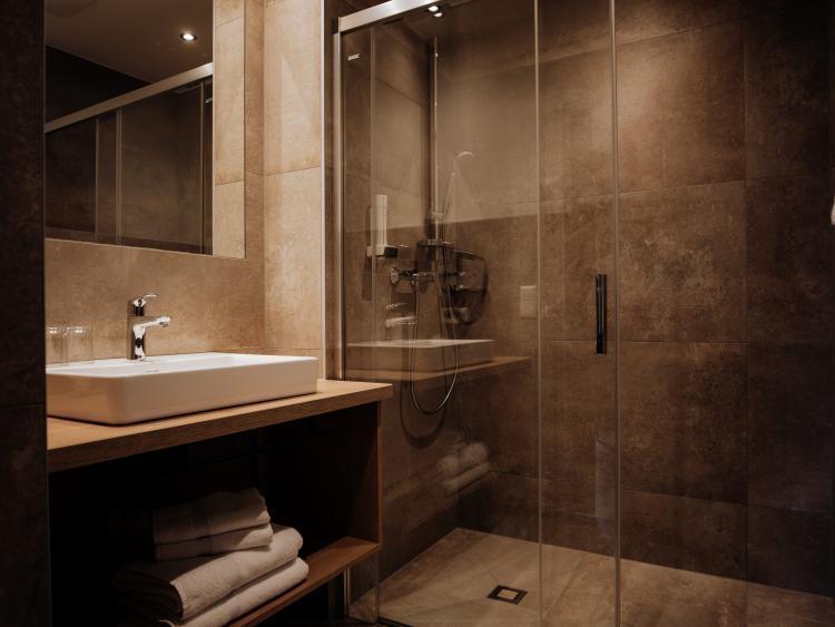 Badezimmer im Hotel Forstauerwirt mit Waschbecken, Spiegel und gläserner Dusche