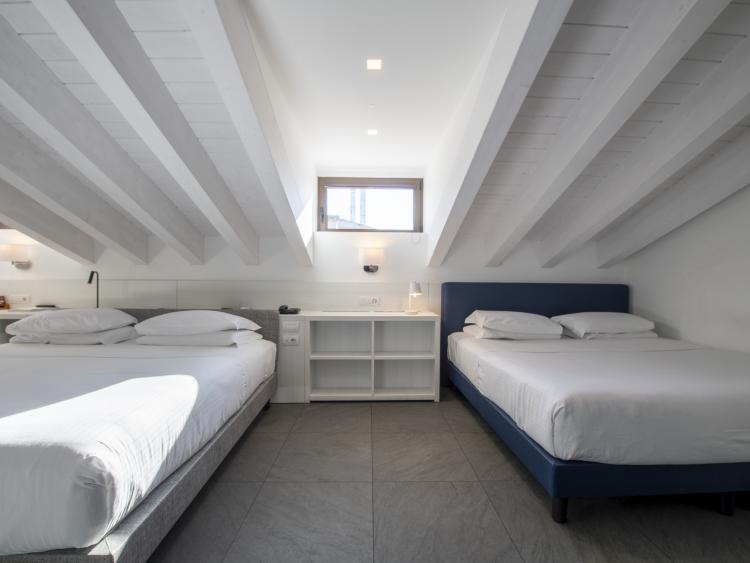 Bright room with two double beds at Hotel Touring Verona under slanted ceiling