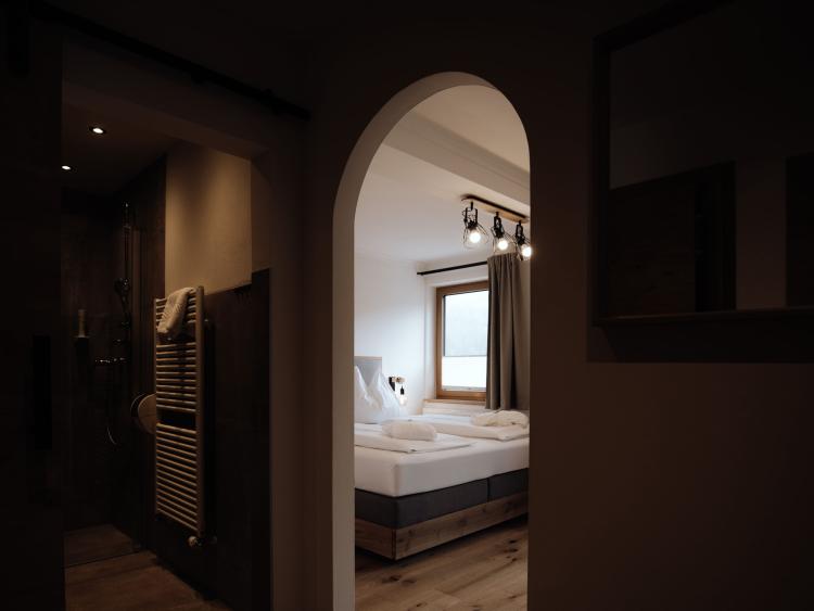 Blick durch einen Rundbogen auf ein helles Zimmer mit Doppelbett im Hotel Forstauerwirt