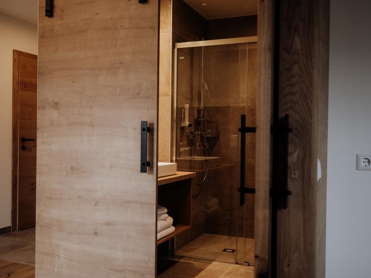 Badezimmer mit Schiebetür aus Holz und Glasdusche im Hotel Forstauerwirt