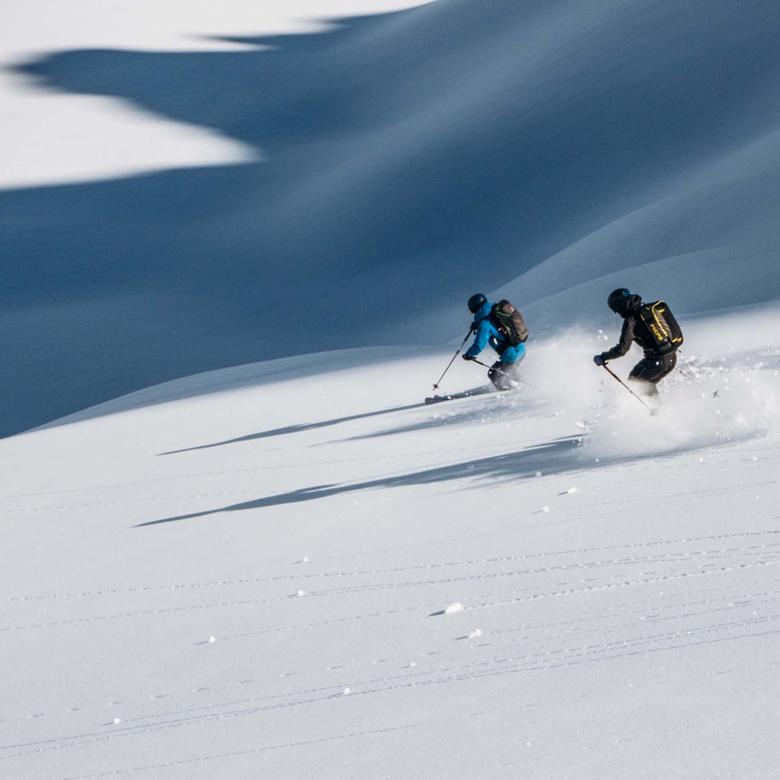 Two skiers skiing on fresh powder snow near Hotel Aurora